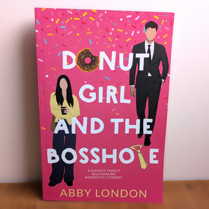 The book cover of 'Donut Girl and the Bosshope' by Abby London, featuring a bright pink background with colorful confetti, a donut, and illustrations of a man in a suit and a woman holding a coffee cup.